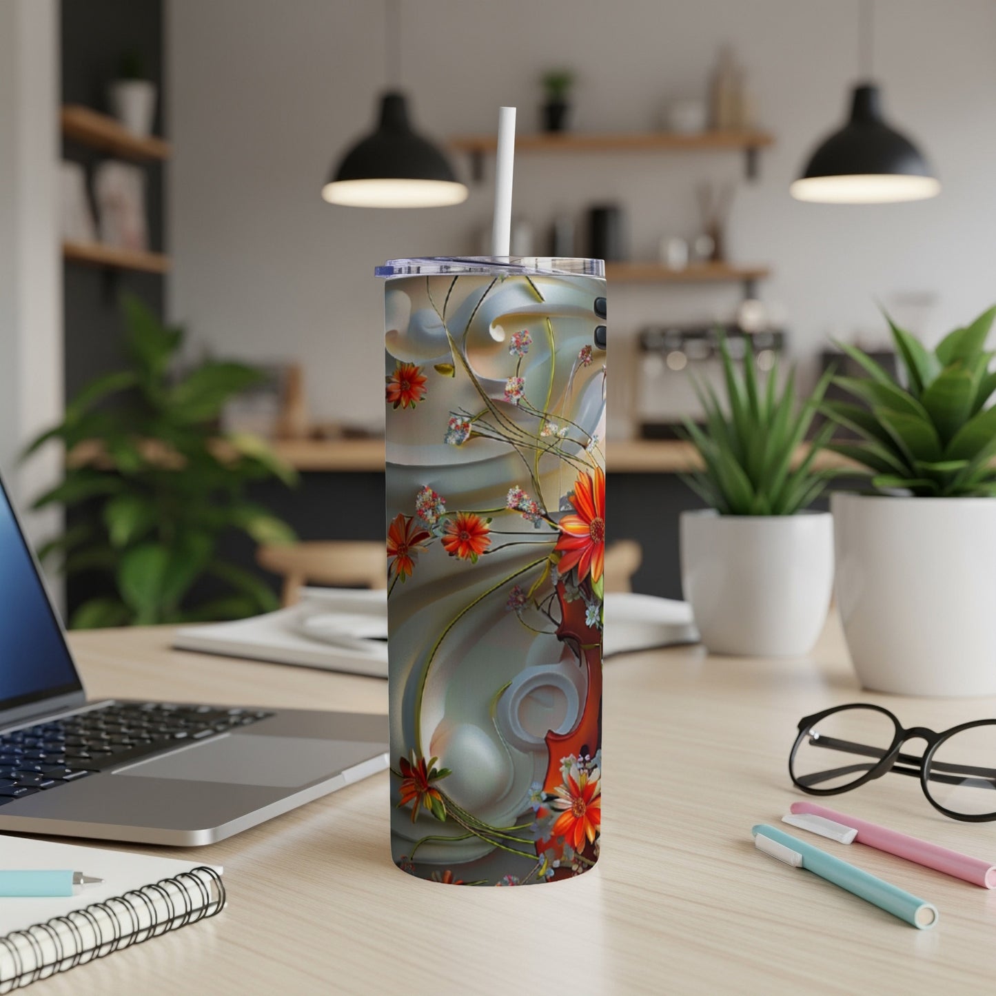 Tall tumbler with floral design on desk with laptop and pens.