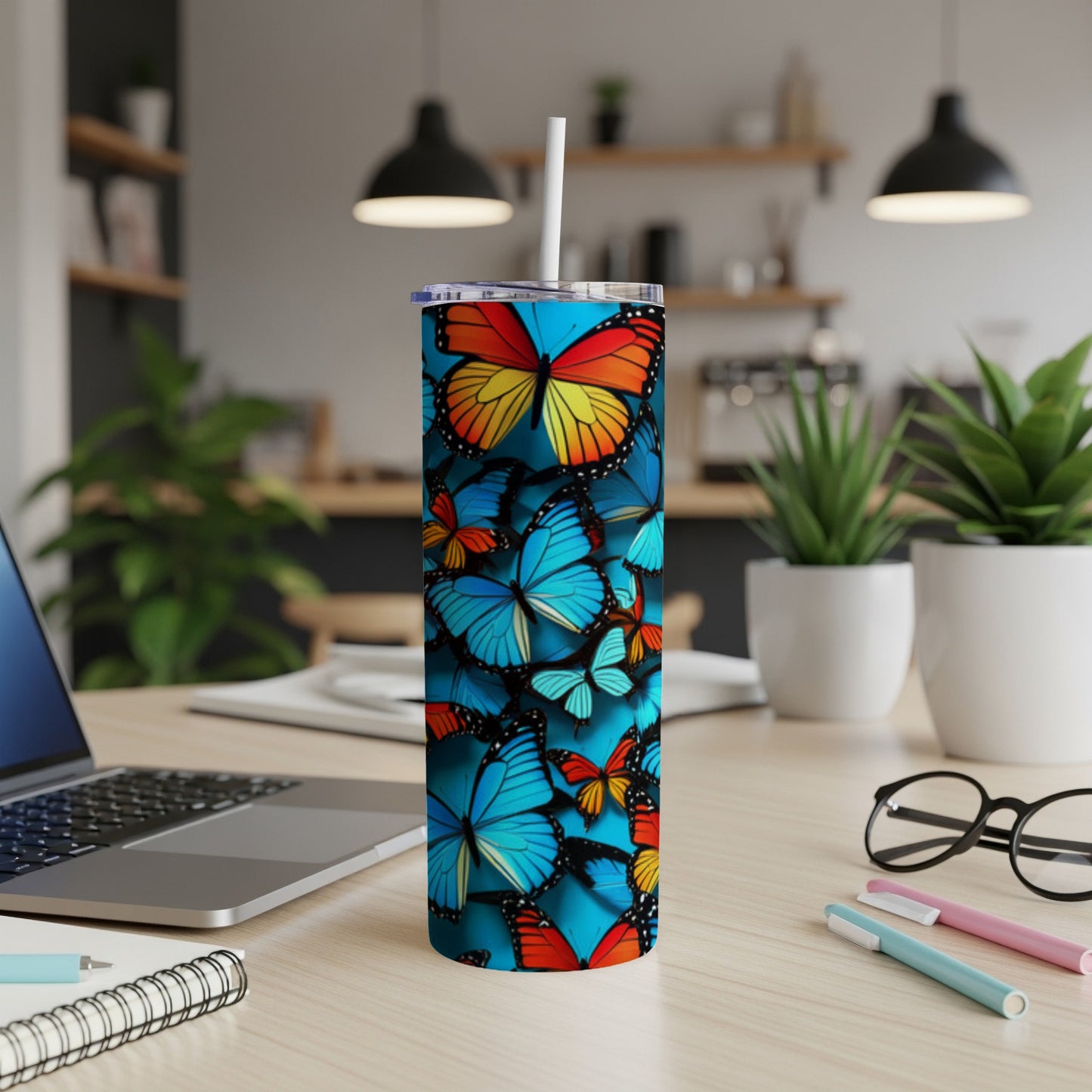 Blue tumbler with colorful butterflies, lid, and straw on a desk.
