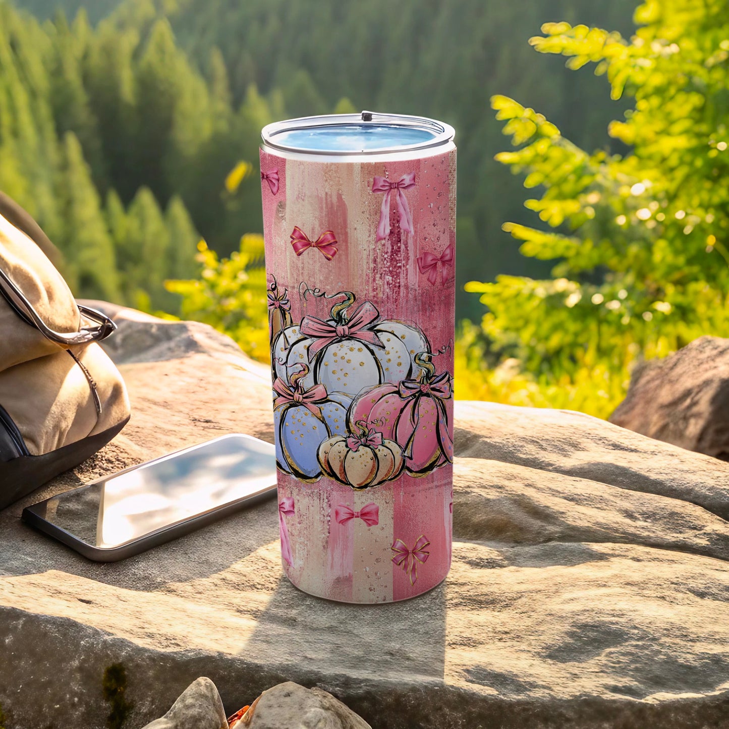 Pink watercolor tumbler with cartoon pumpkins and bows, outdoor setting.