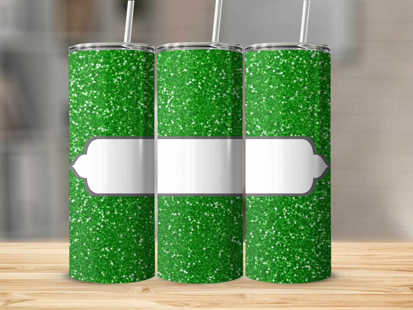 Three green glitter tumblers with white label and straws on a wooden surface.