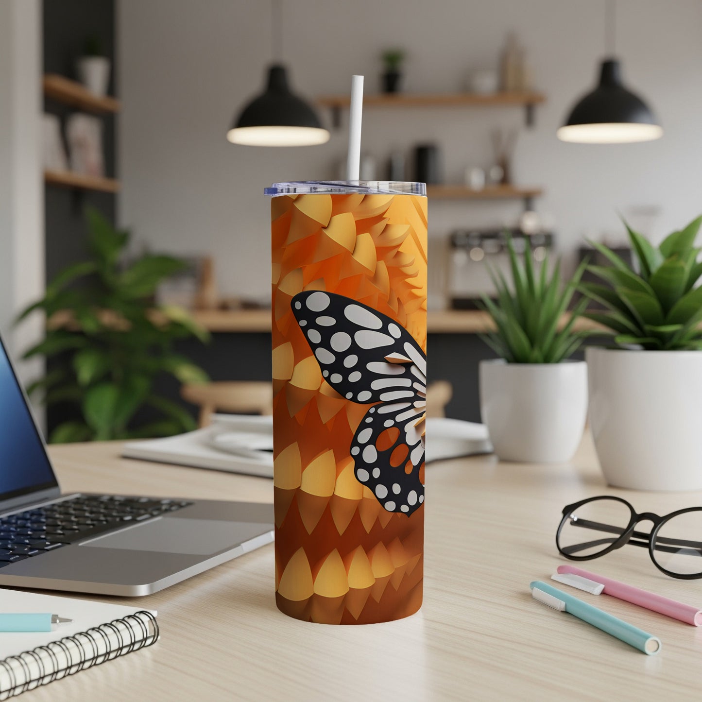 Tall tumbler with a butterfly design and straw on a desk.