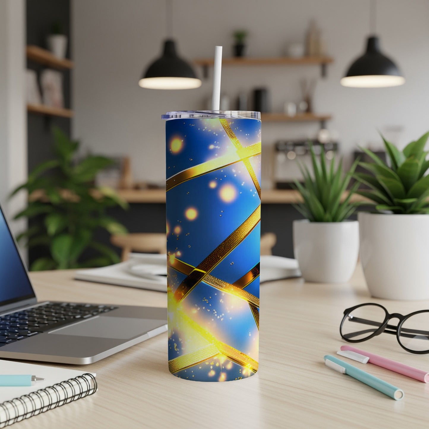 Blue tumbler with gold ribbon and sparkles, on a desk.