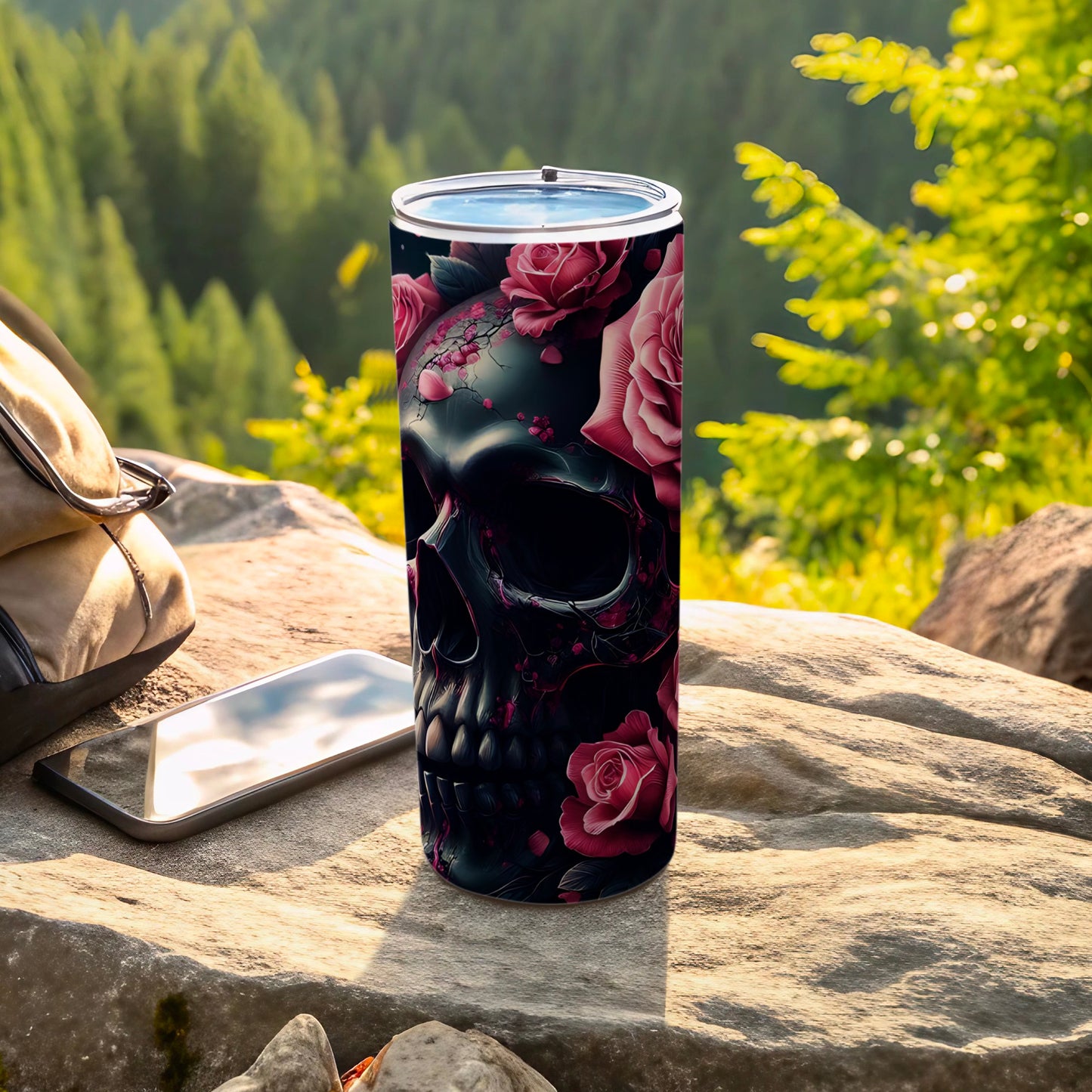 Black skull with pink roses design on a tumbler, next to a phone and backpack.