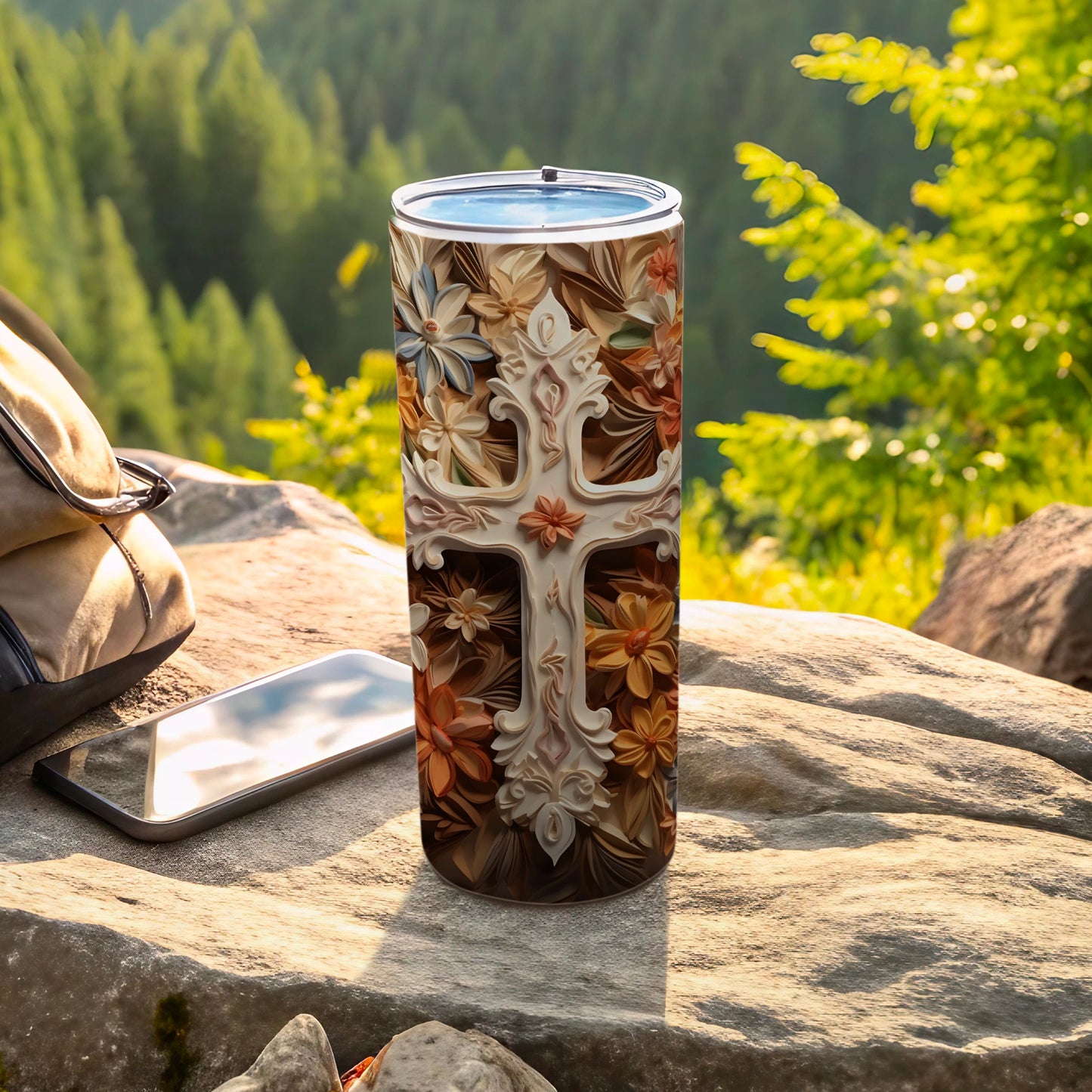 Tumbler with a carved cross and floral design, outdoors on rocks.