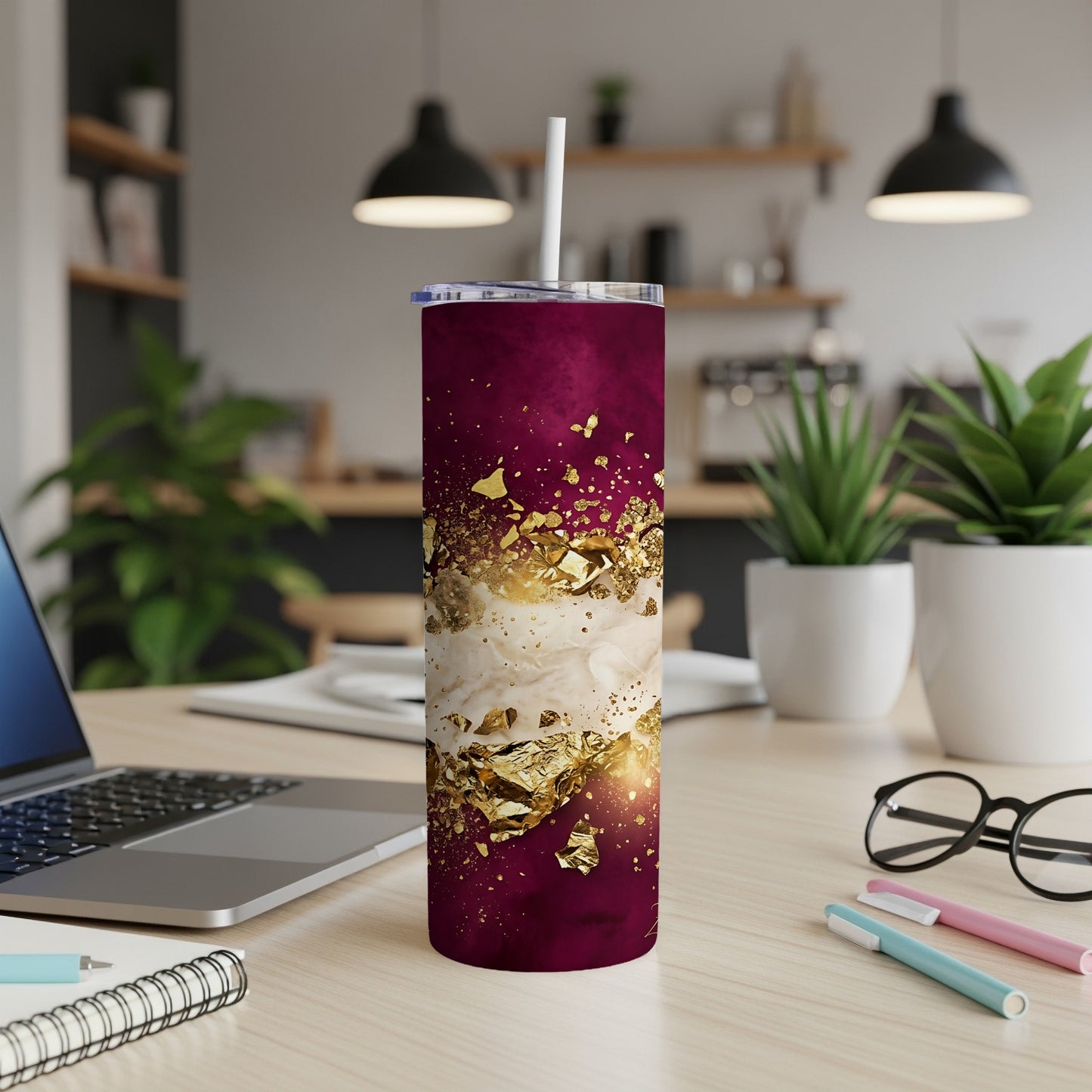 Maroon and gold splatter pattern stainless steel tumbler with straw on desk.
