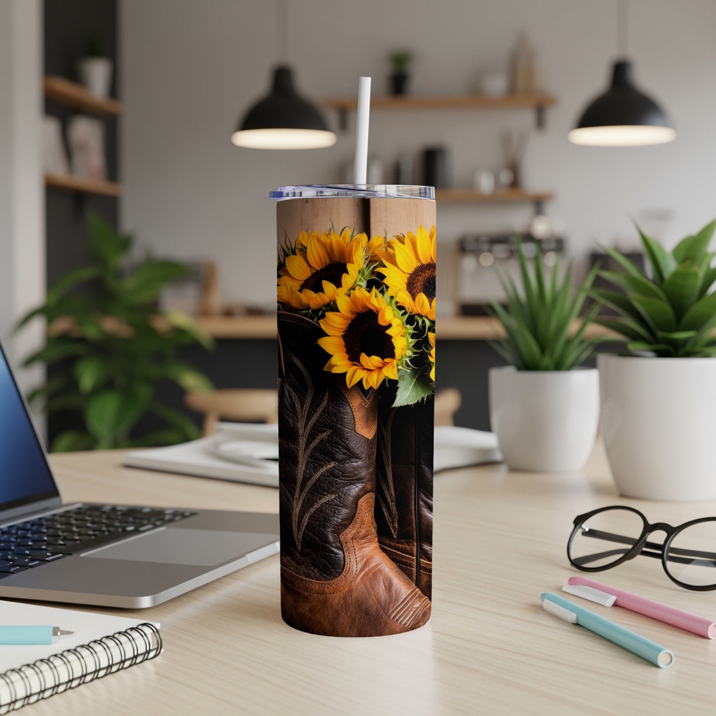 Brown leather cowboy boots with sunflowers on a desk next to a laptop.