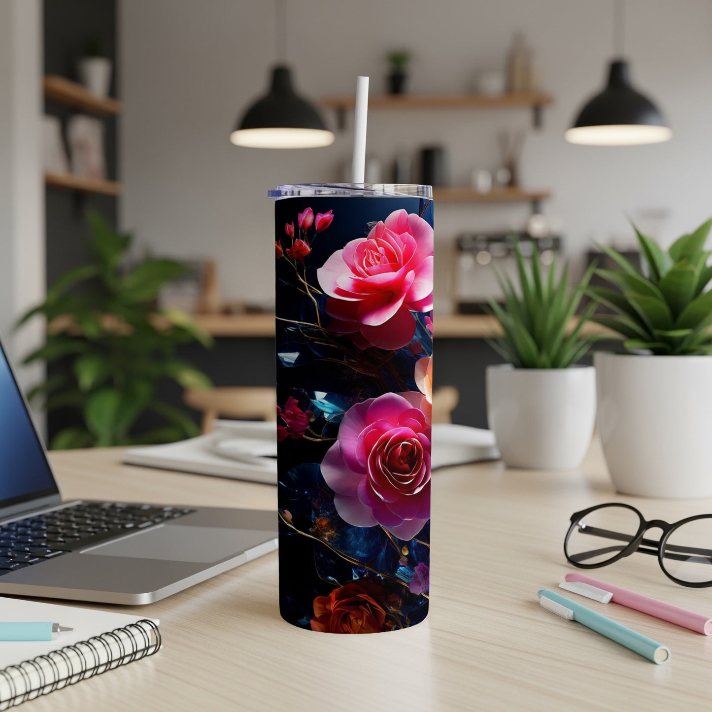 Floral tumbler with pink roses on a desk with a laptop and pens.