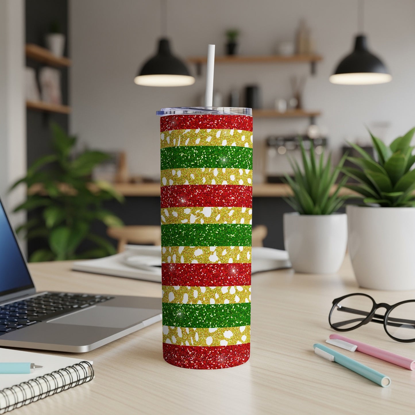 Glittery red, gold, and green striped tumbler with a white straw on a desk.
