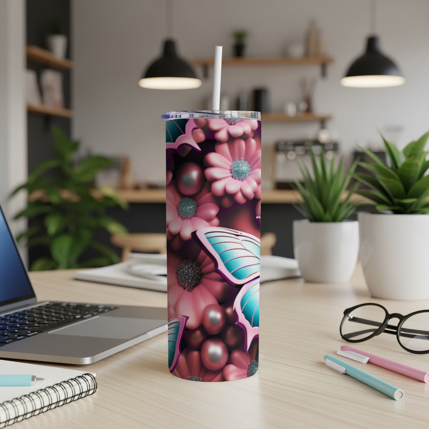 Pink floral and butterfly tumbler on a desk with a laptop and pens.