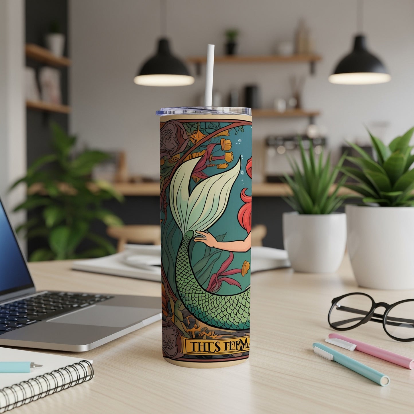 Tumbler with mermaid illustration and straw, on a desk.