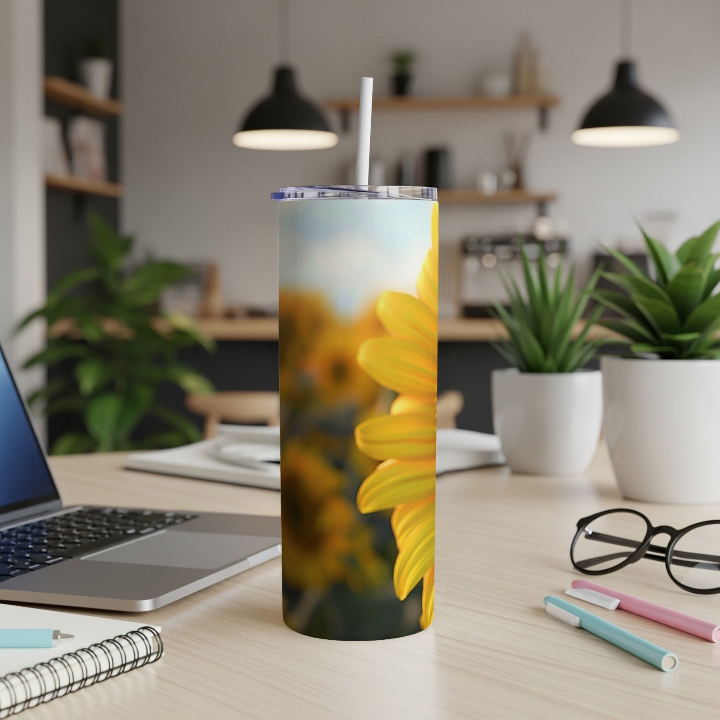 Tall tumbler with sunflower pattern on a desk with laptop and pens.