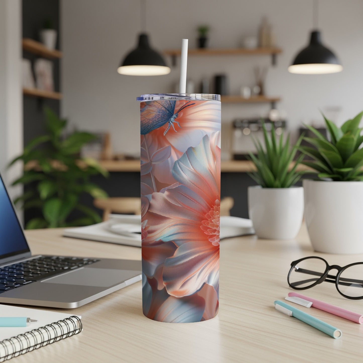 Floral tumbler with butterfly and straw on a desk.