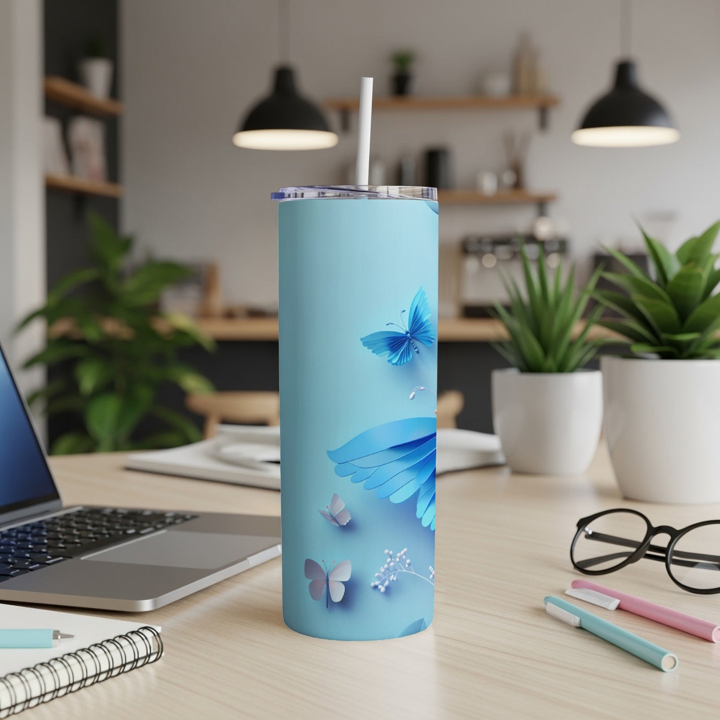 Light blue tumbler with butterfly designs and a straw, on a desk.