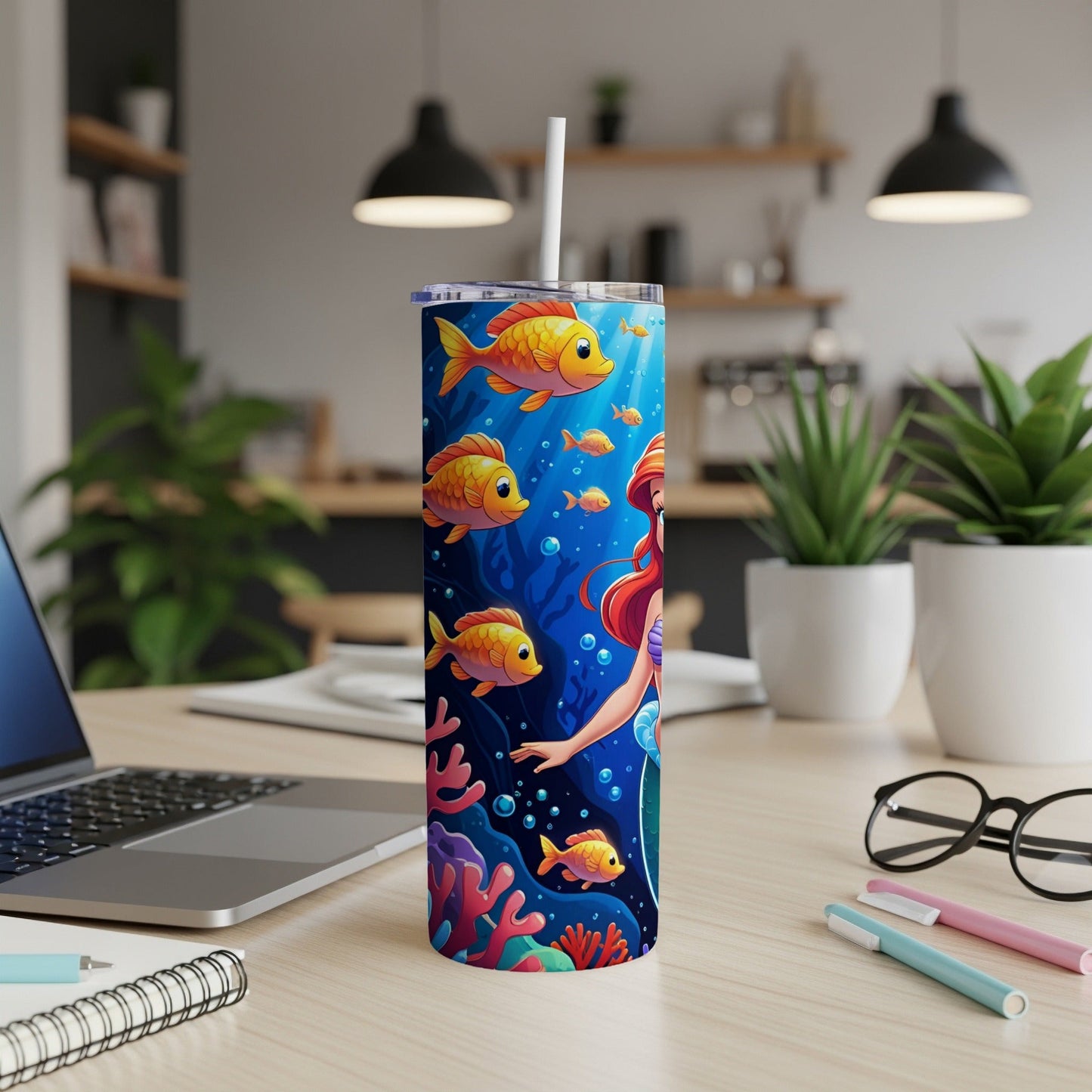Mermaid and fish on a tumbler on a desk with laptop and pens.