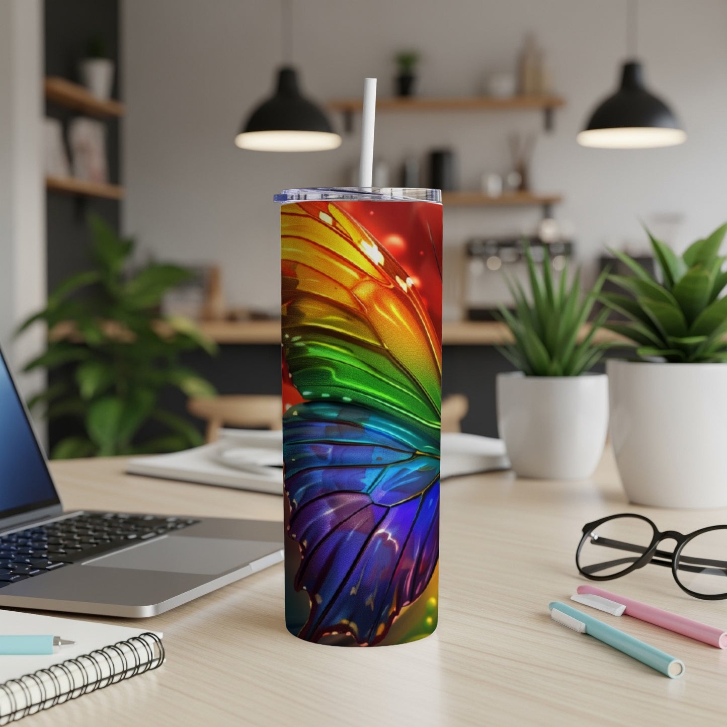 Rainbow butterfly tumbler with straw on a desk with a laptop and pens.