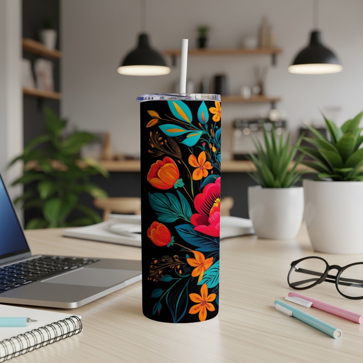 Black tumbler with vibrant floral pattern, white straw, sits on a desk.