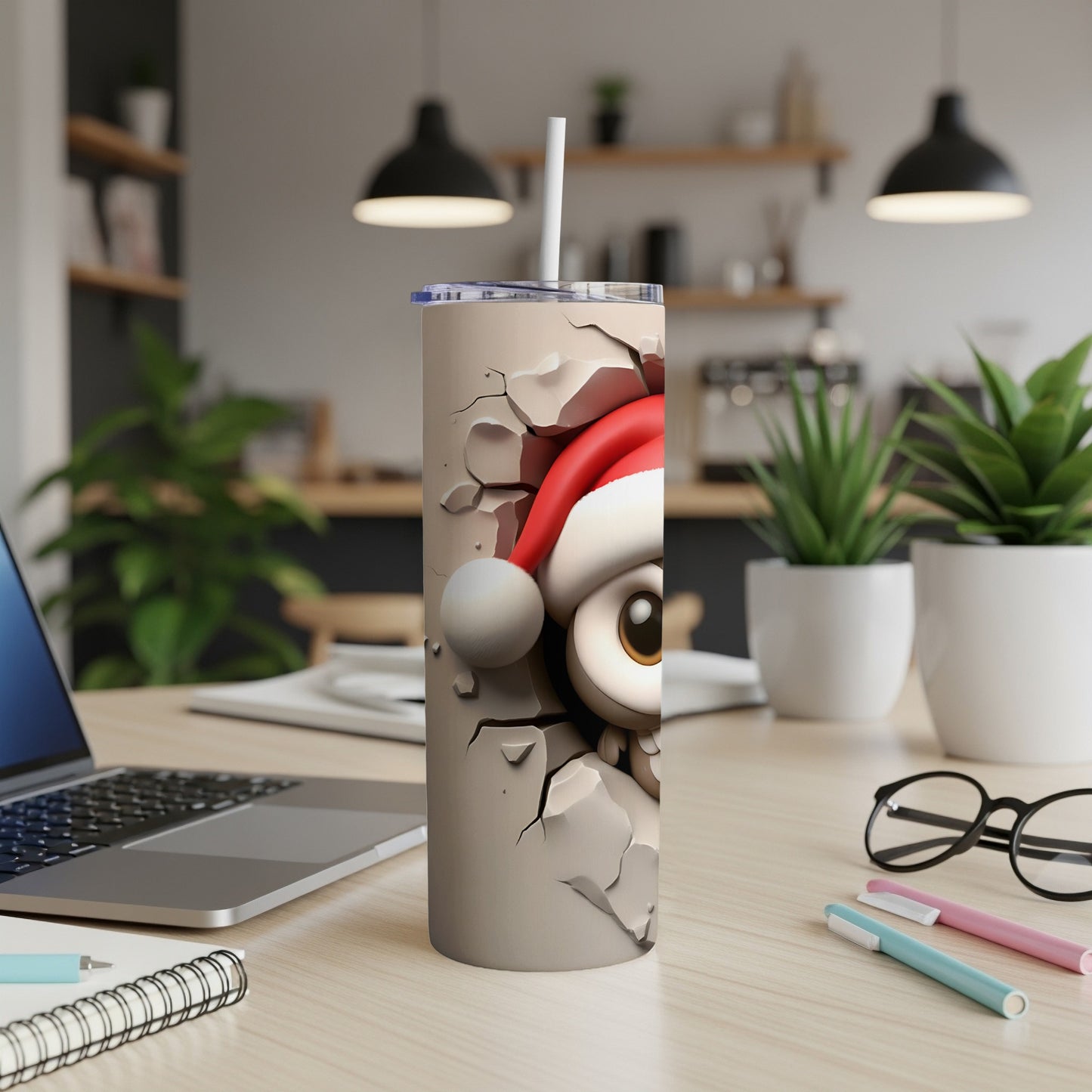 Cracked tumbler with cartoon eye, Santa hat, and straw on a desk.