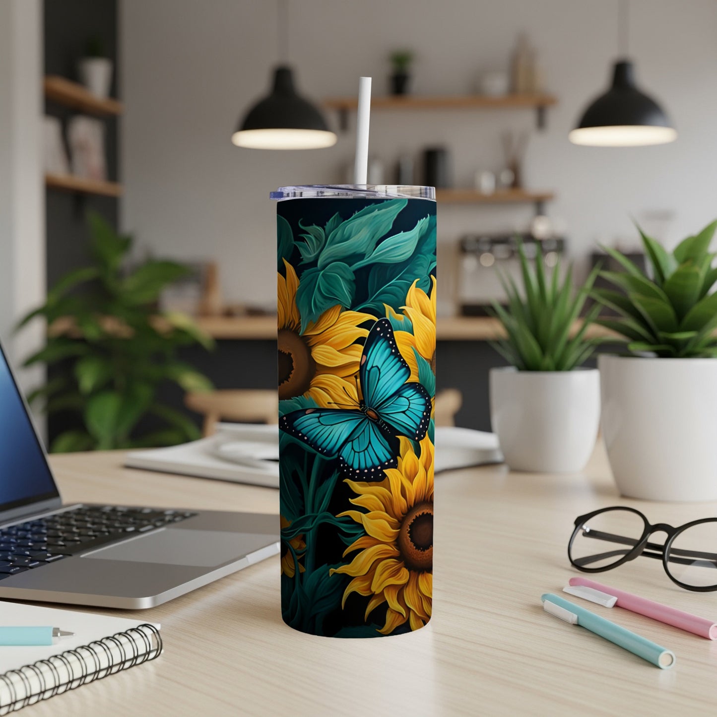 Tall tumbler with sunflowers and a blue butterfly on a desk.