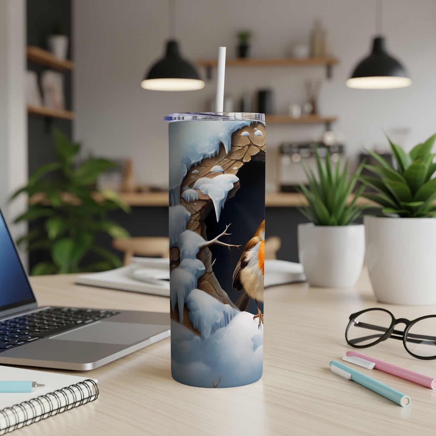 Snow-covered branch with robin, on a tumbler with a laptop and pens.