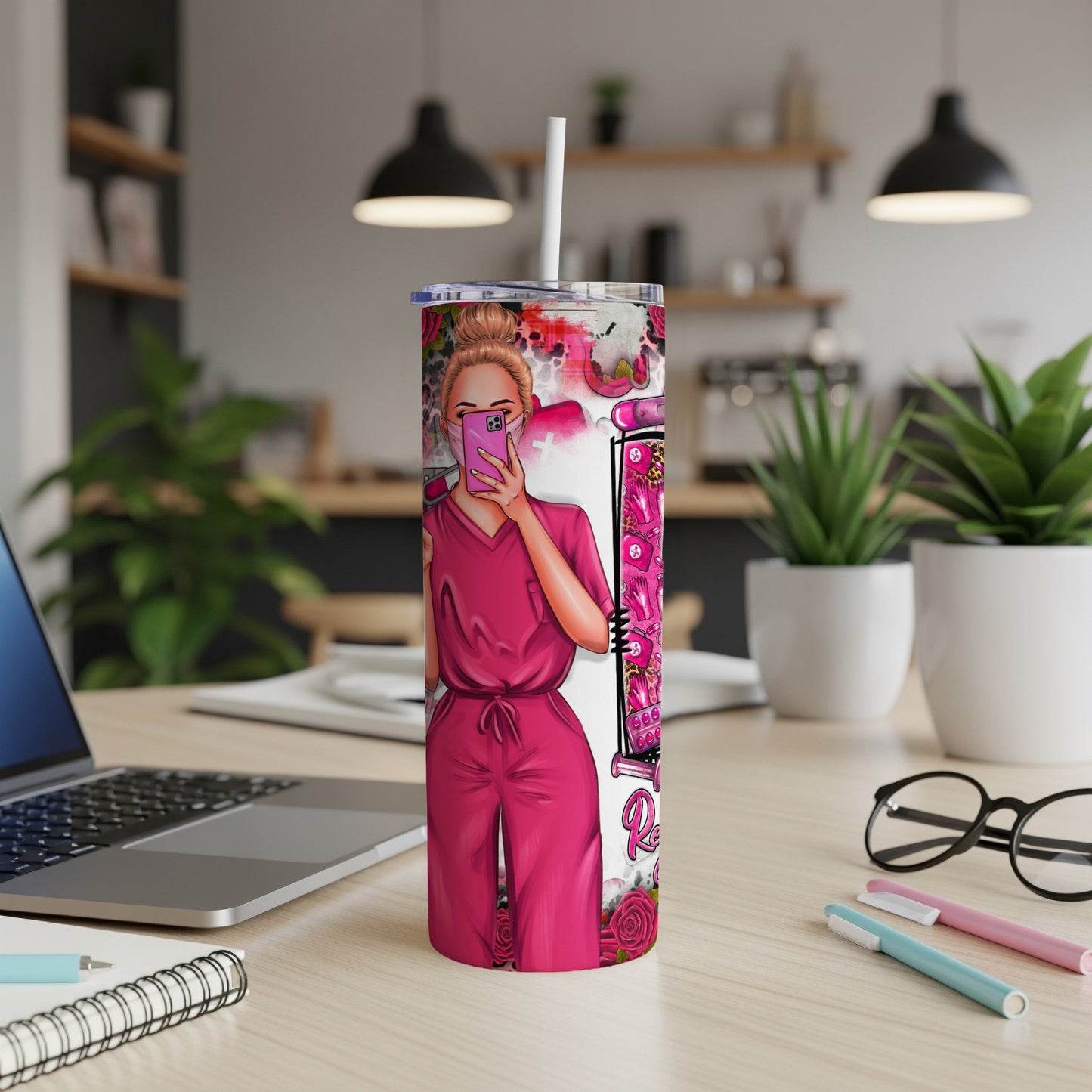 Pink tumbler with nurse illustration, holding phone, pink scrub uniform, laptop, and pens.