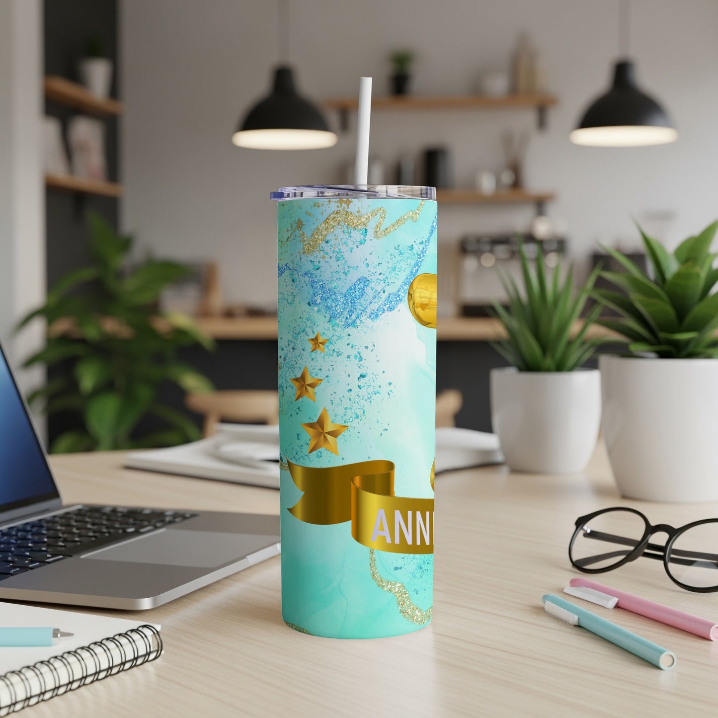 Turquoise tumbler with gold stars and "ANNIVERSARY" text on desk.