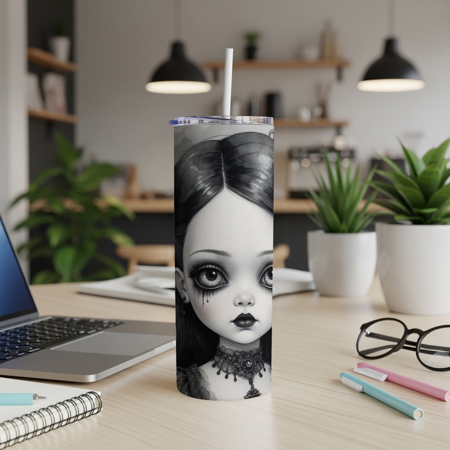 Gothic doll illustration on a tumbler with a laptop and office supplies.