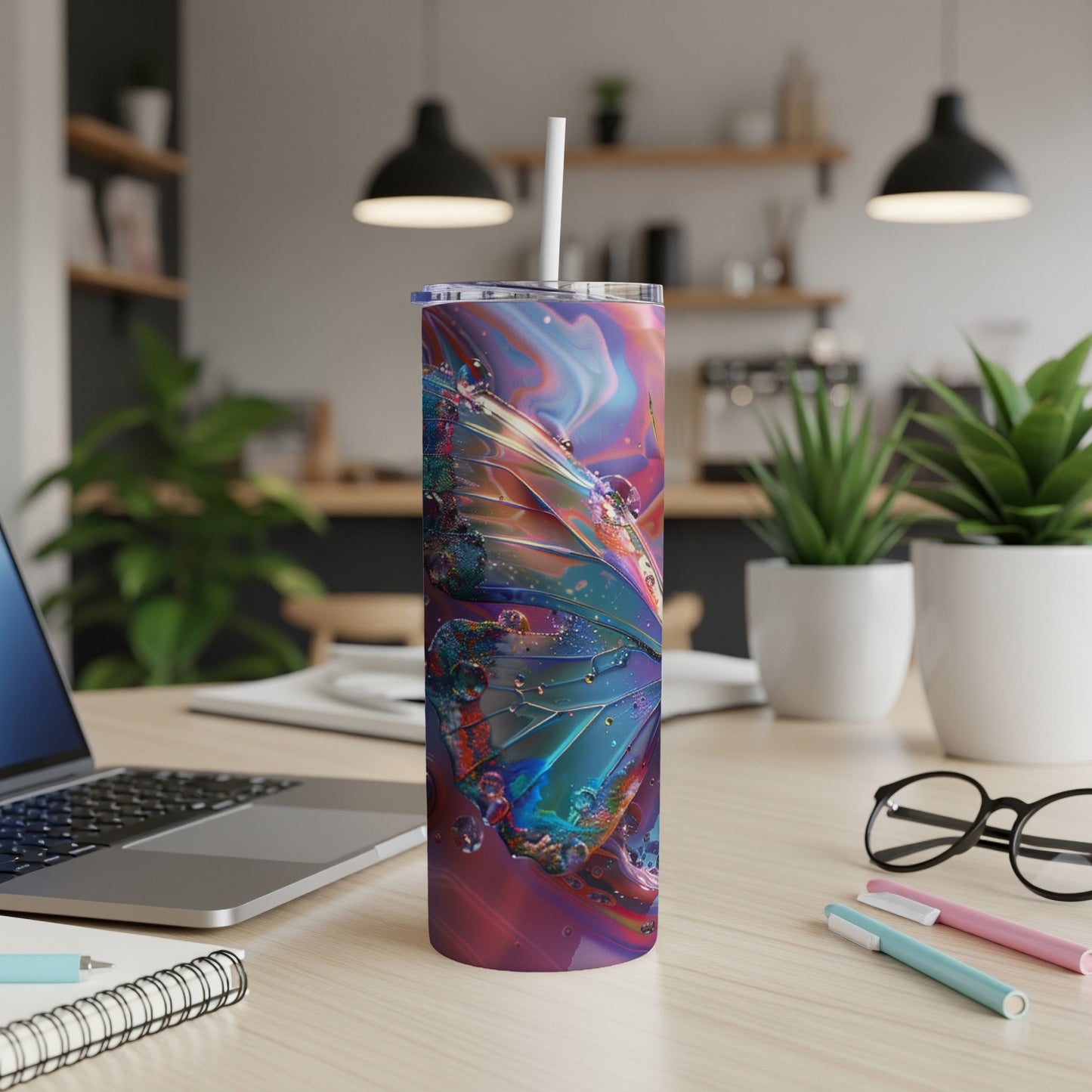 Colorful butterfly tumbler with straw on a desk with laptop and pens.
