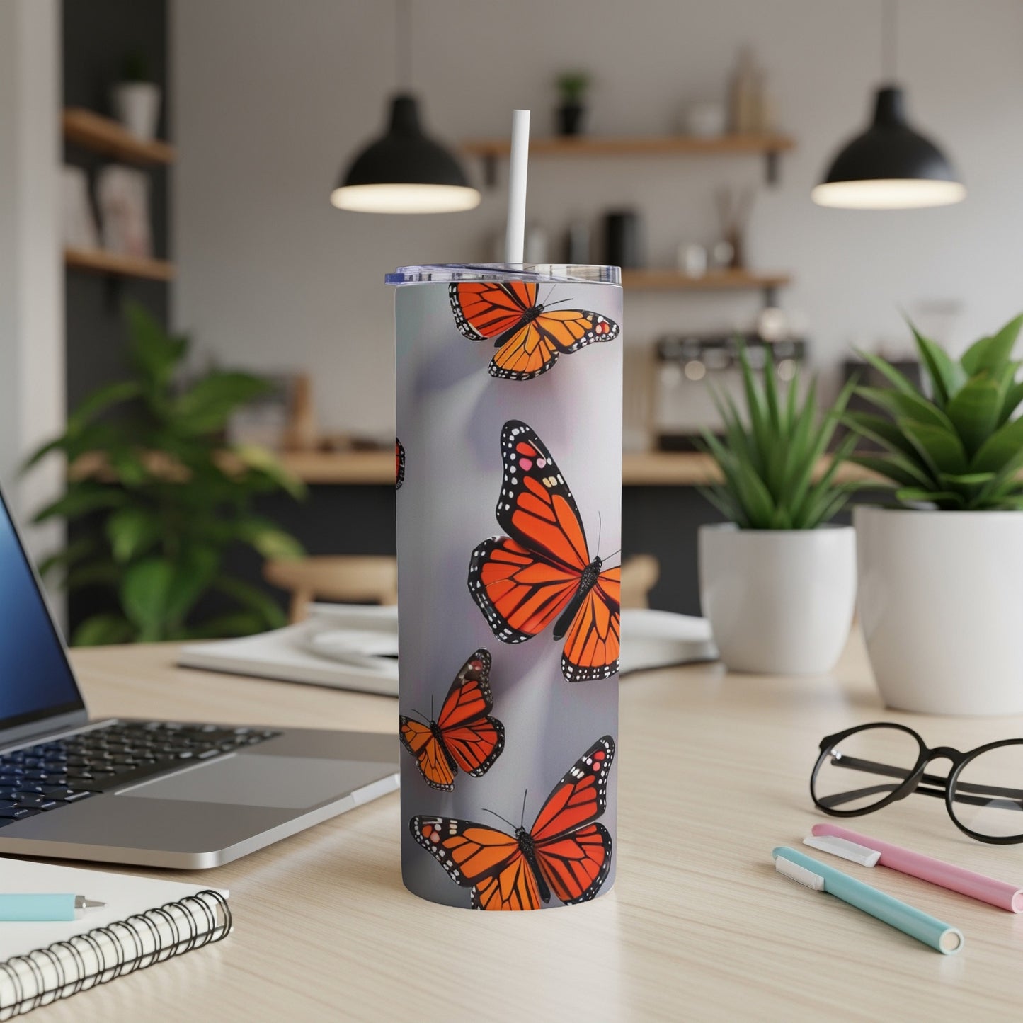 Monarch butterflies scattered across a silver tumbler with a white straw.