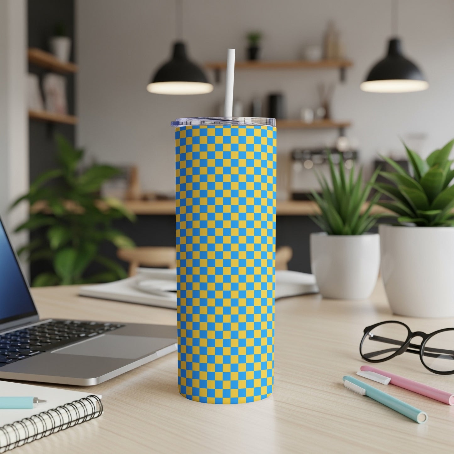 Blue and yellow checkered tumbler with straw on a desk.