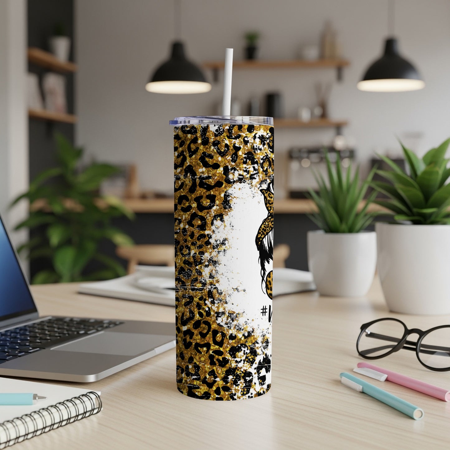 Leopard print tumbler with white straw on desk next to laptop.