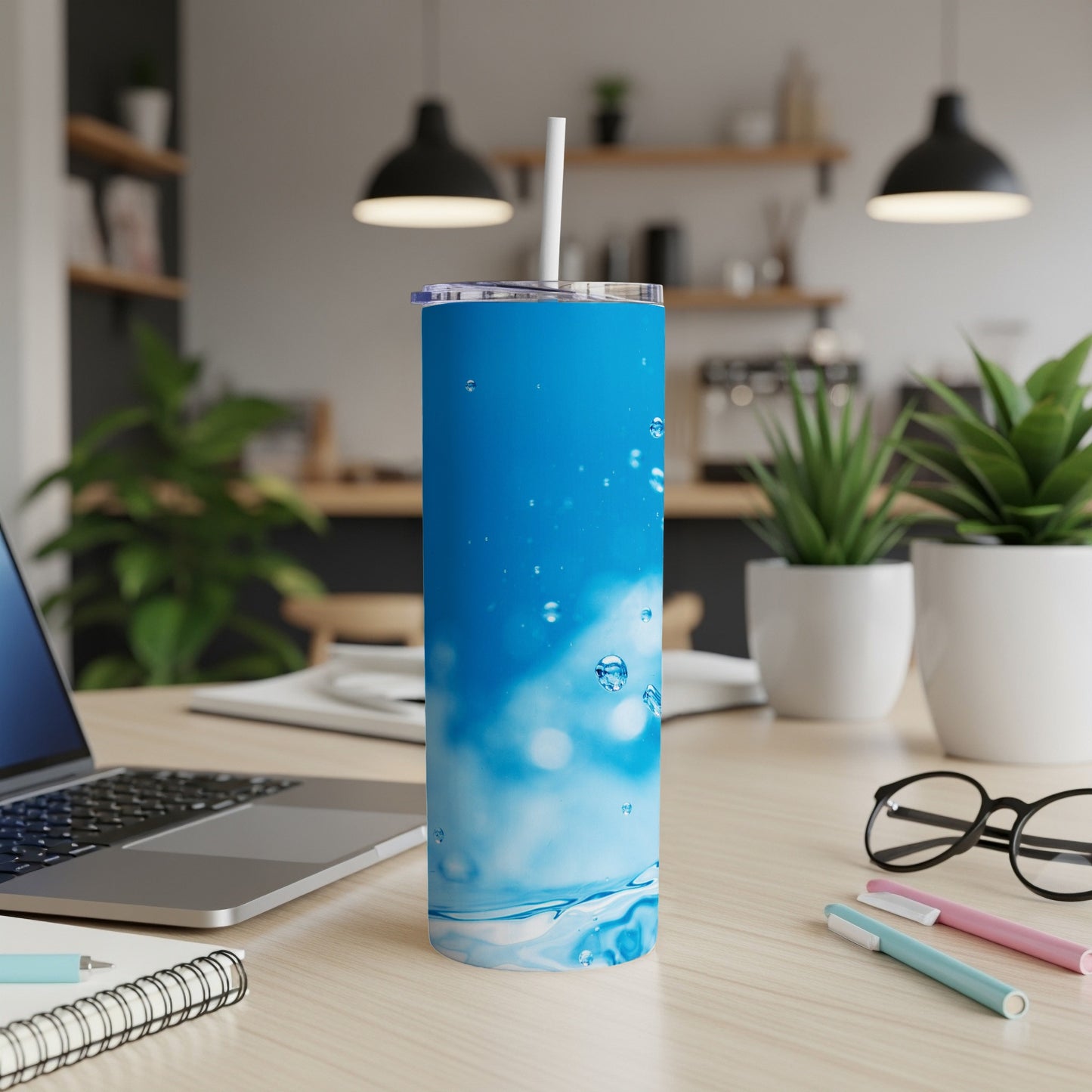 Blue tumbler with water bubbles design and straw, on a desk.