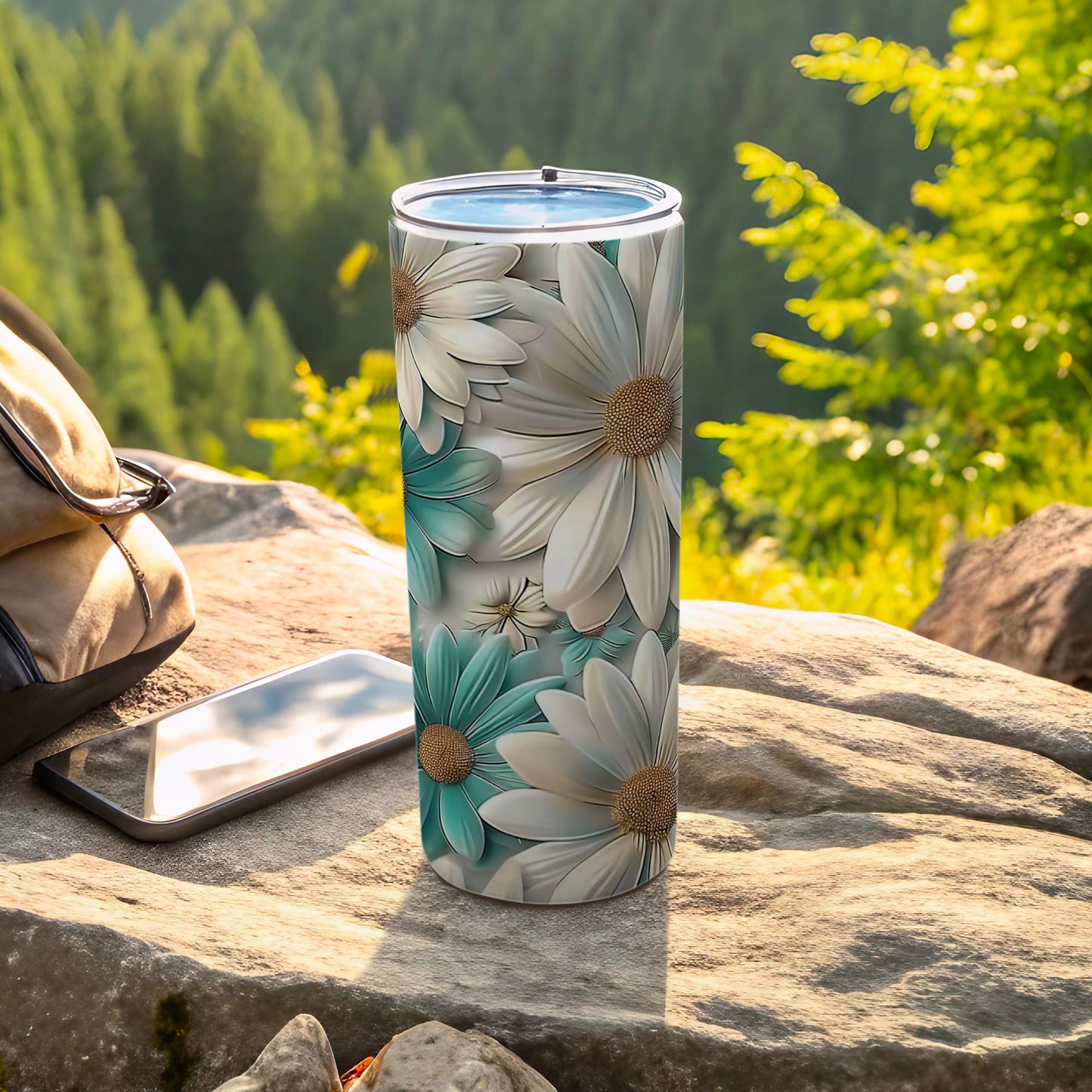 Tumbler with white and teal daisy pattern on a rocky surface.
