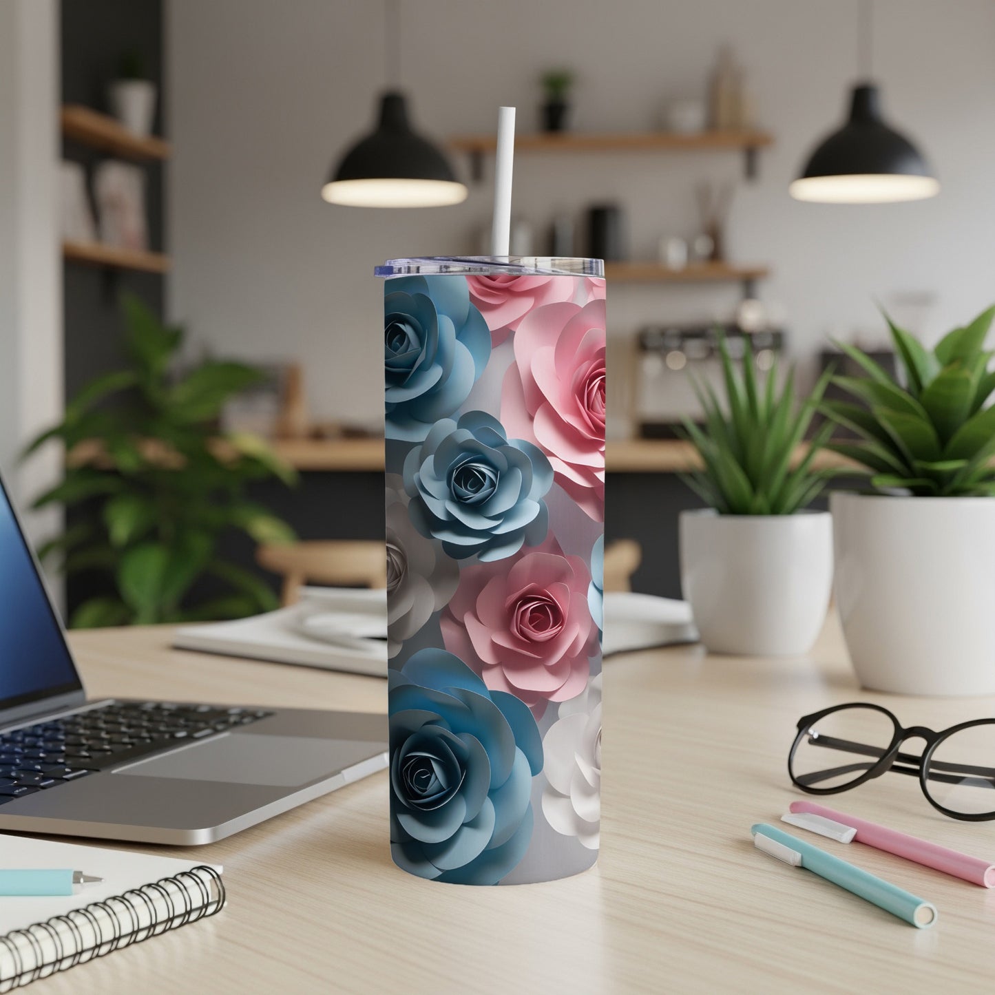 Tall tumbler with pink and blue paper flowers, on a desk with laptop and pens.