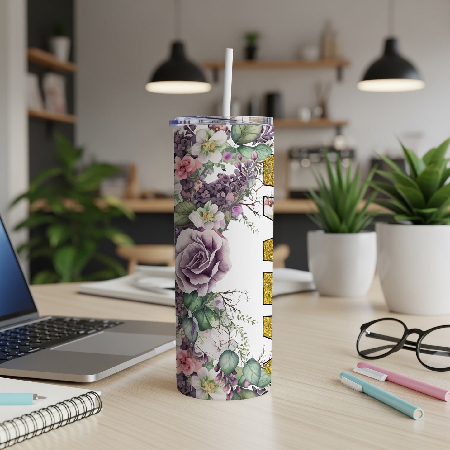 Floral tumbler with white lid and straw on a wooden desk.