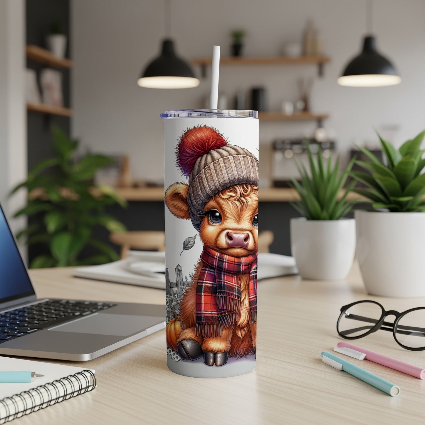 Tumbler with a cartoon cow wearing a hat and scarf on a desk.
