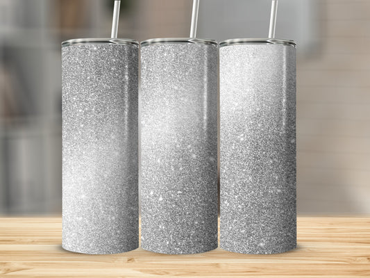 Three silver glitter tumblers with white straws on a wooden surface.