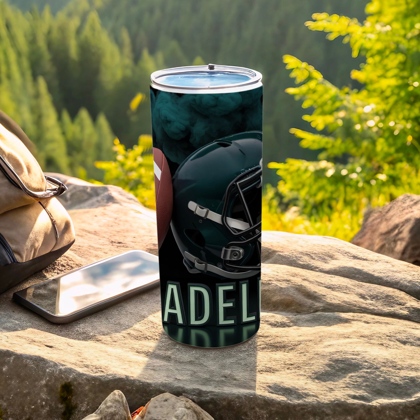 Football helmet and "ADEL" text on a tumbler, outdoors.