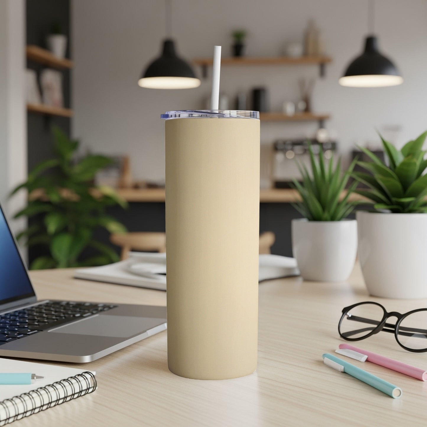 Tan tumbler with white straw on a desk with laptop and pens.