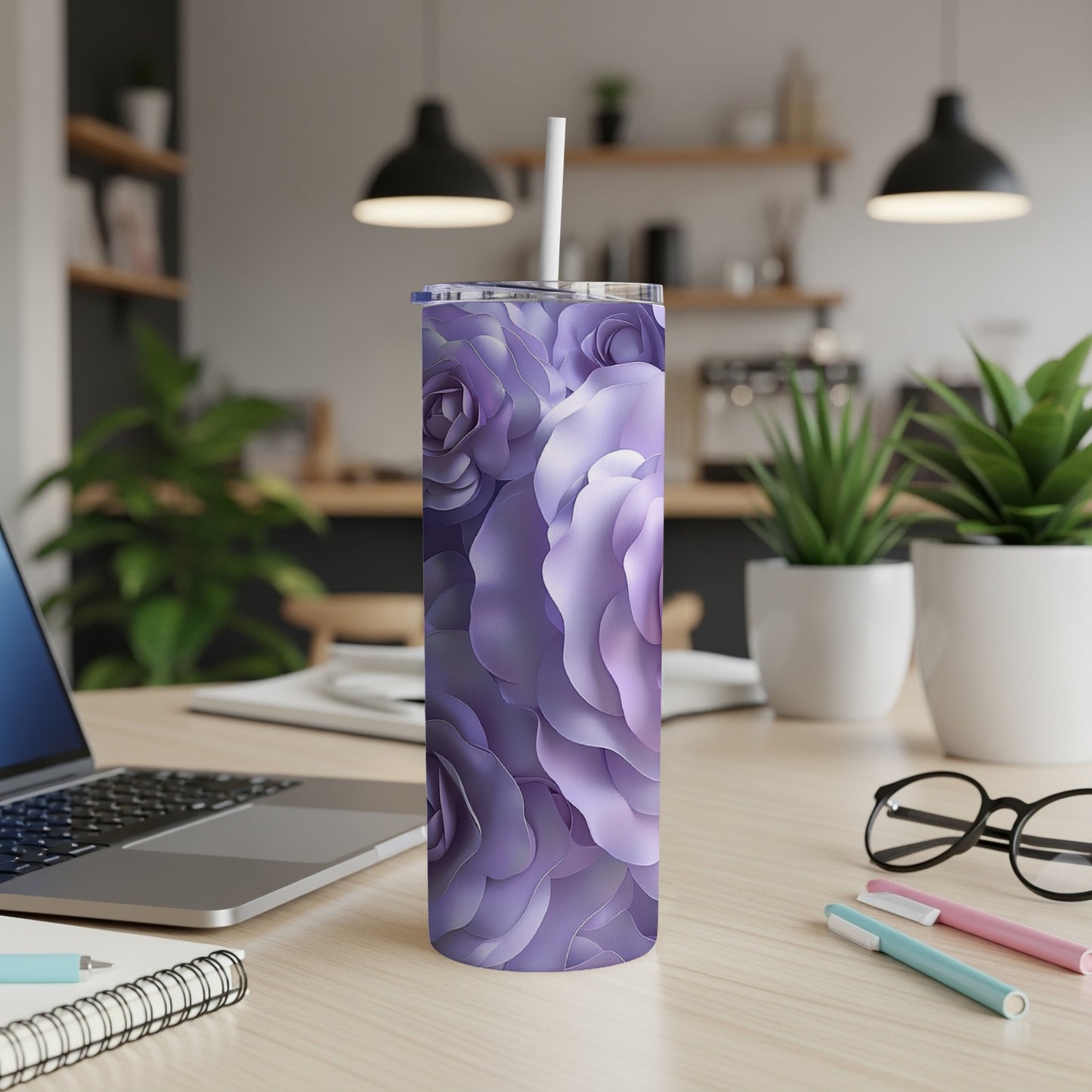 Purple floral tumbler with straw on a desk with a laptop and pens.