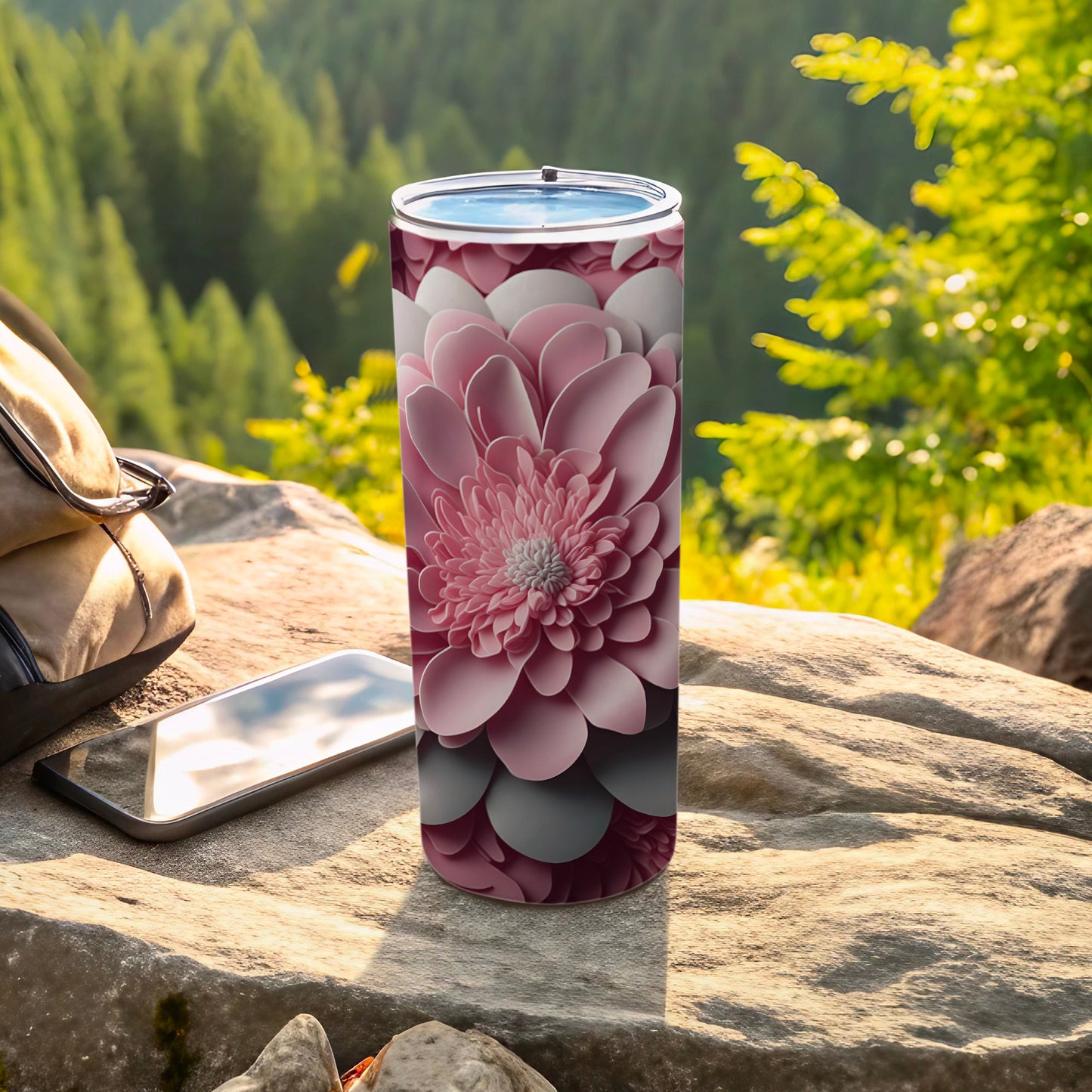 Pink floral patterned tumbler on rock with phone and backpack.