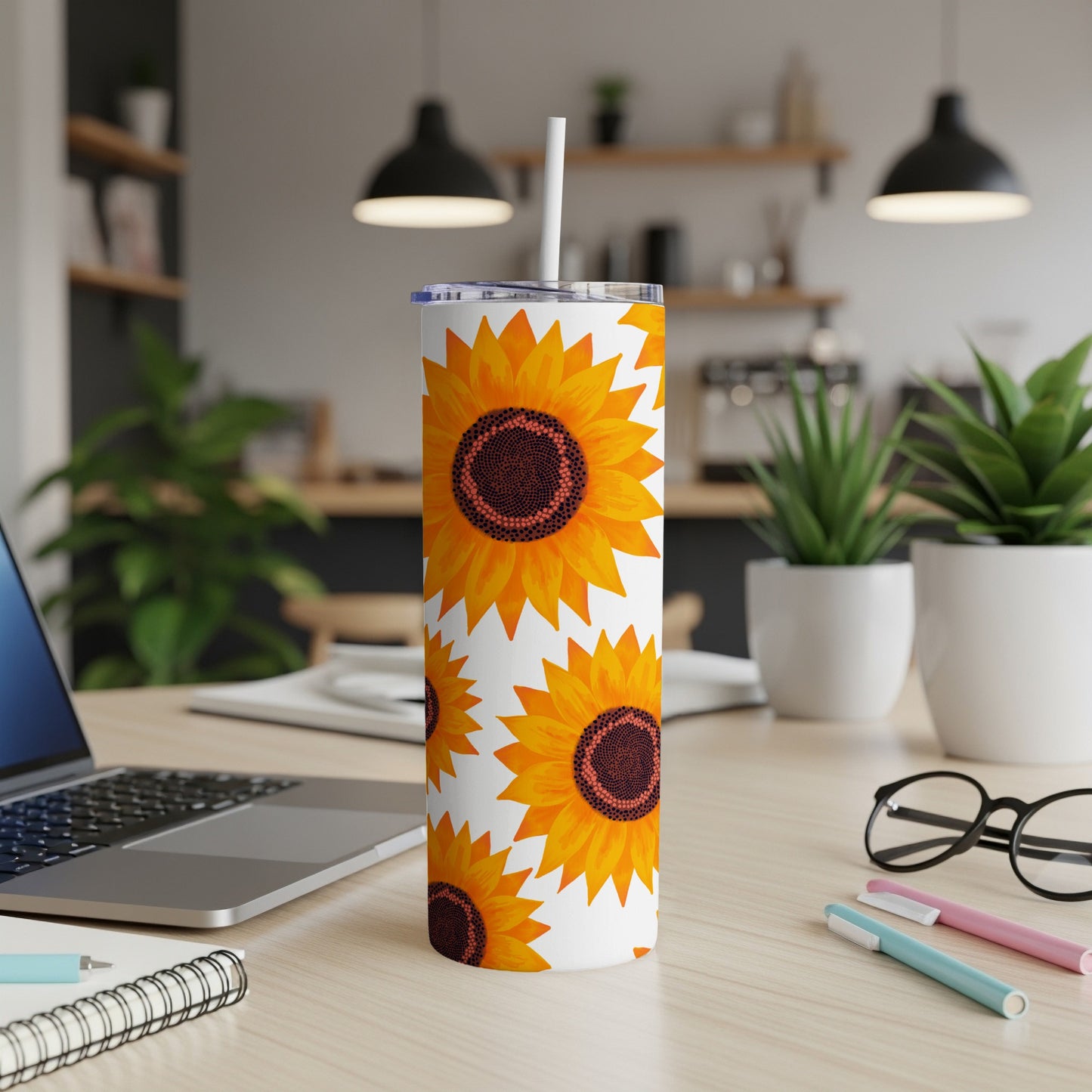 White tumbler with repeating sunflower pattern and straw, on a desk.