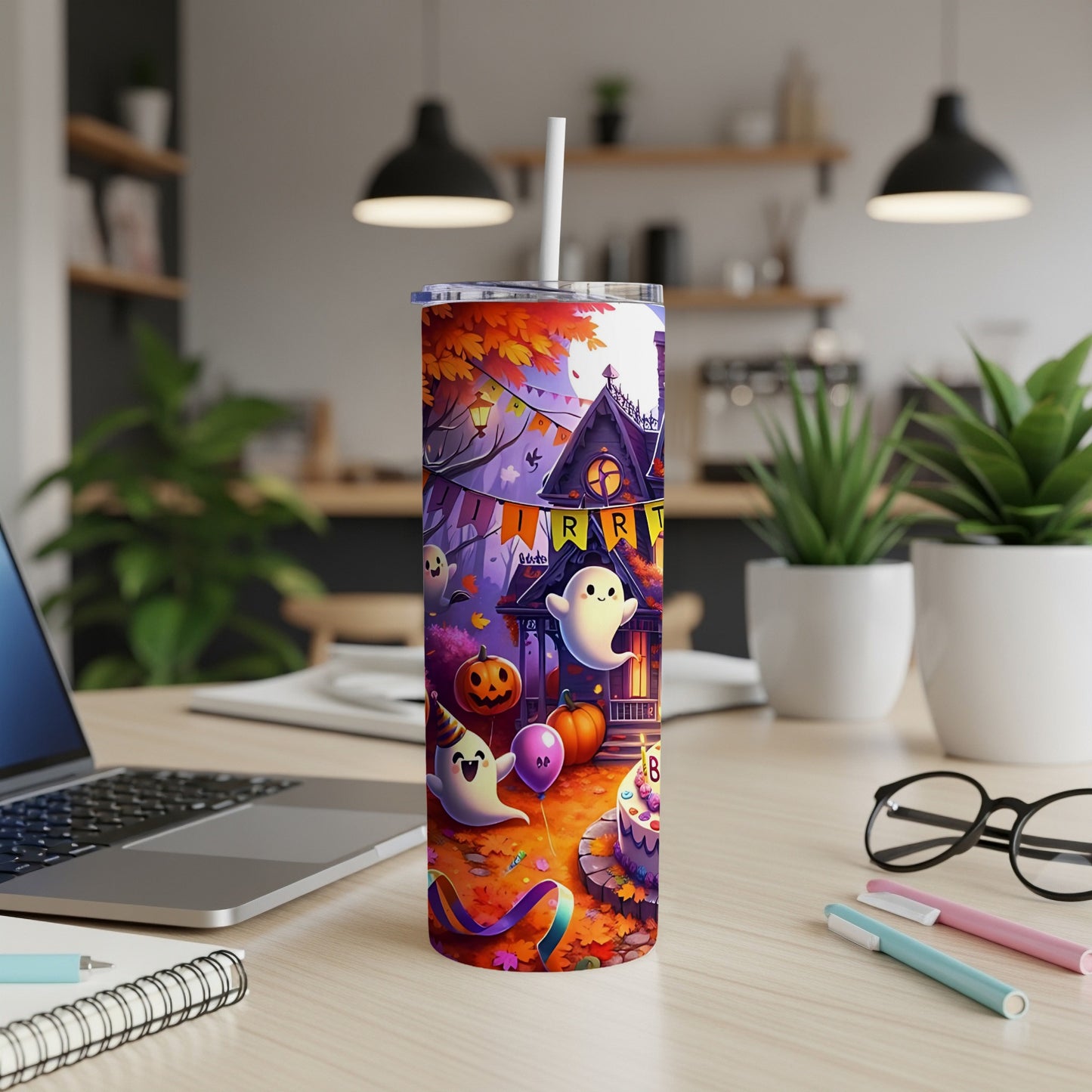 Halloween tumbler with ghosts, pumpkins, and a haunted house on a desk.