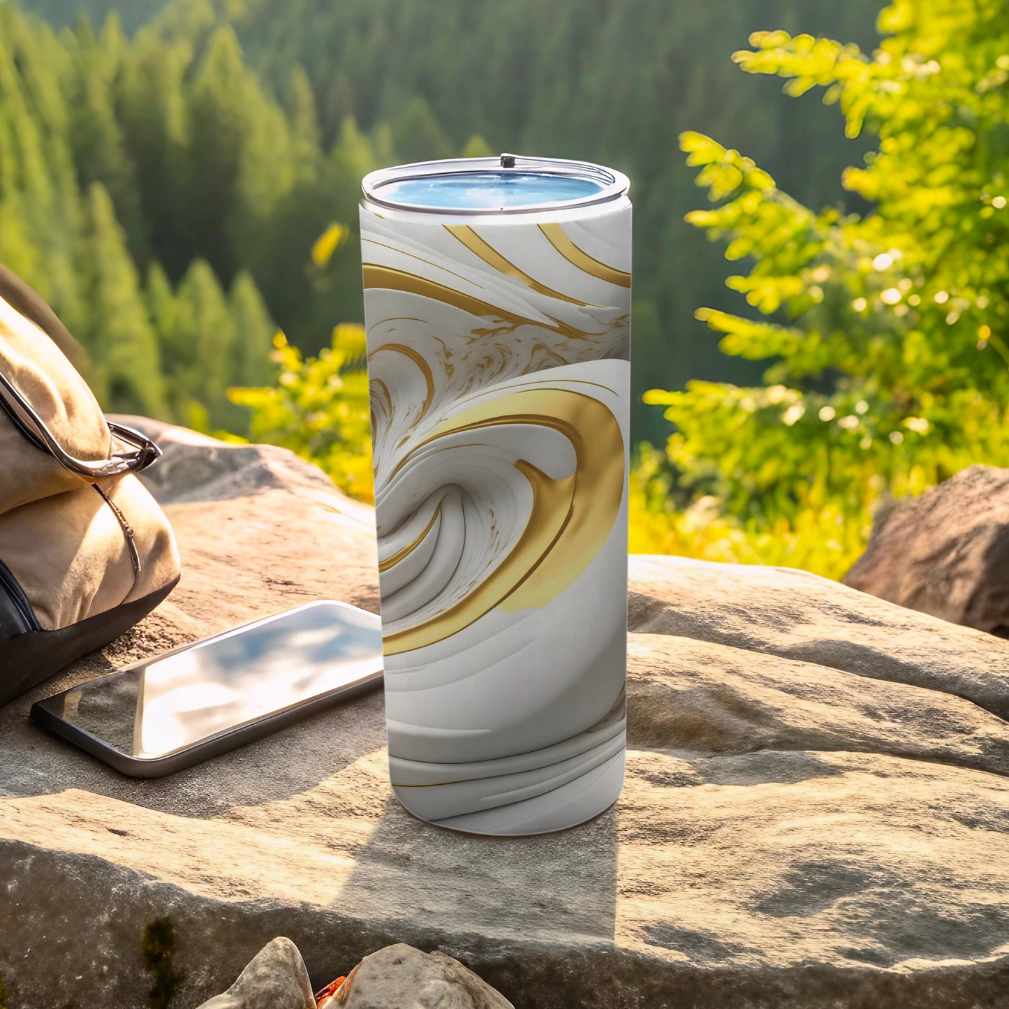 White and gold marbled tumbler sits on rocks with a phone and backpack.