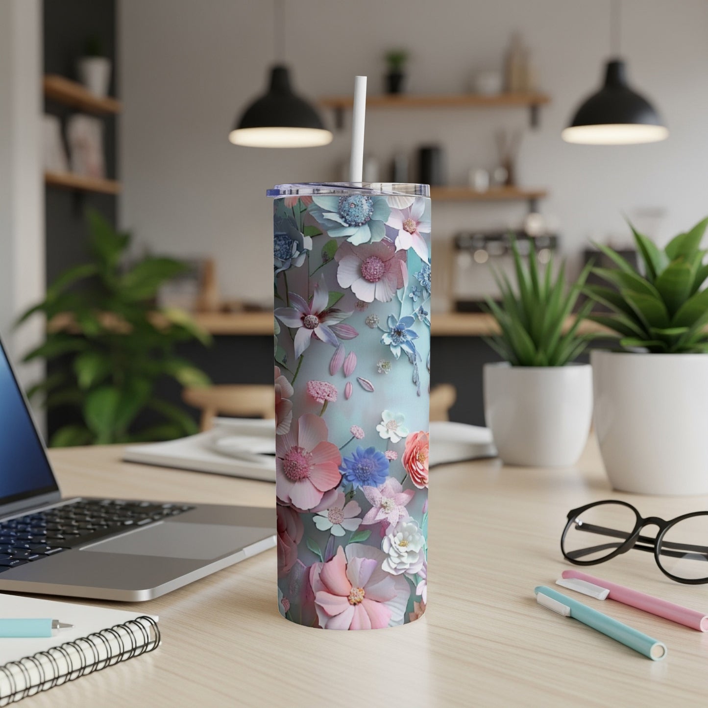 Floral tumbler with straw on desk with laptop and pens.