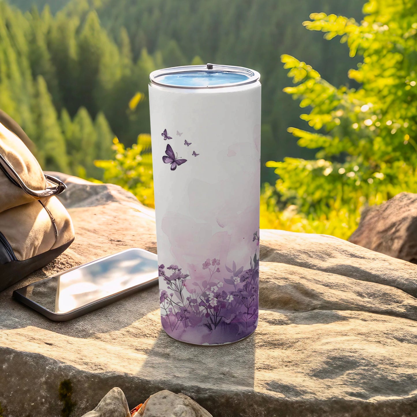White tumbler with purple floral and butterfly design on outdoor rock setting.