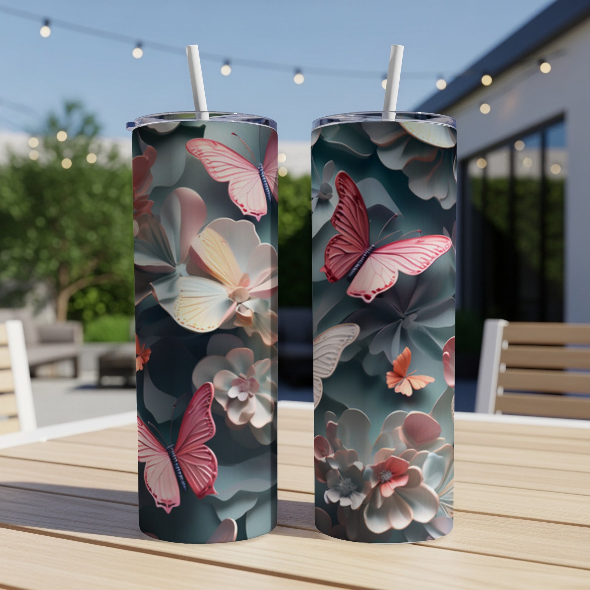 Two tall tumblers with pink butterflies and floral designs on an outdoor table.