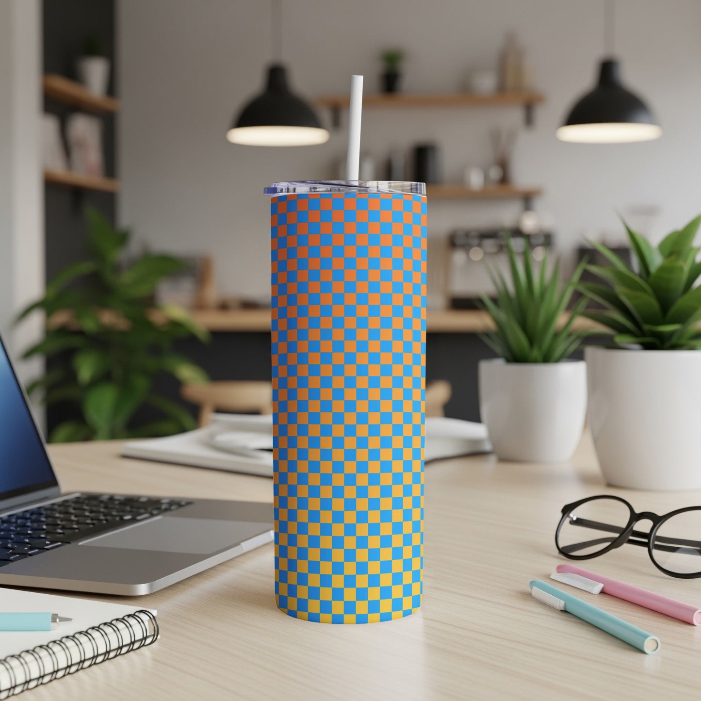 Orange and blue checkered tumbler with a straw on a desk.