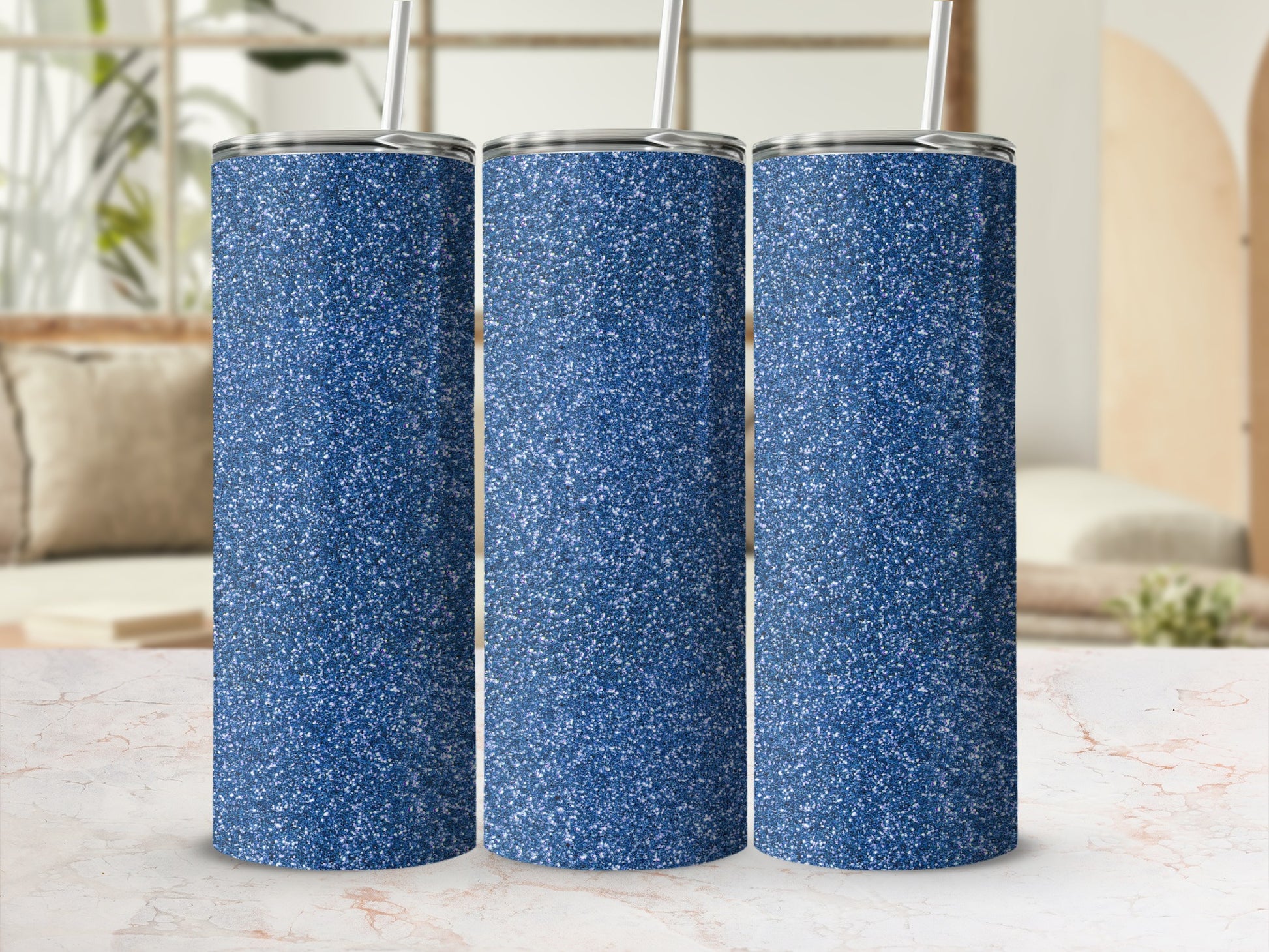 Three blue glitter tumblers with straws on a marble surface.