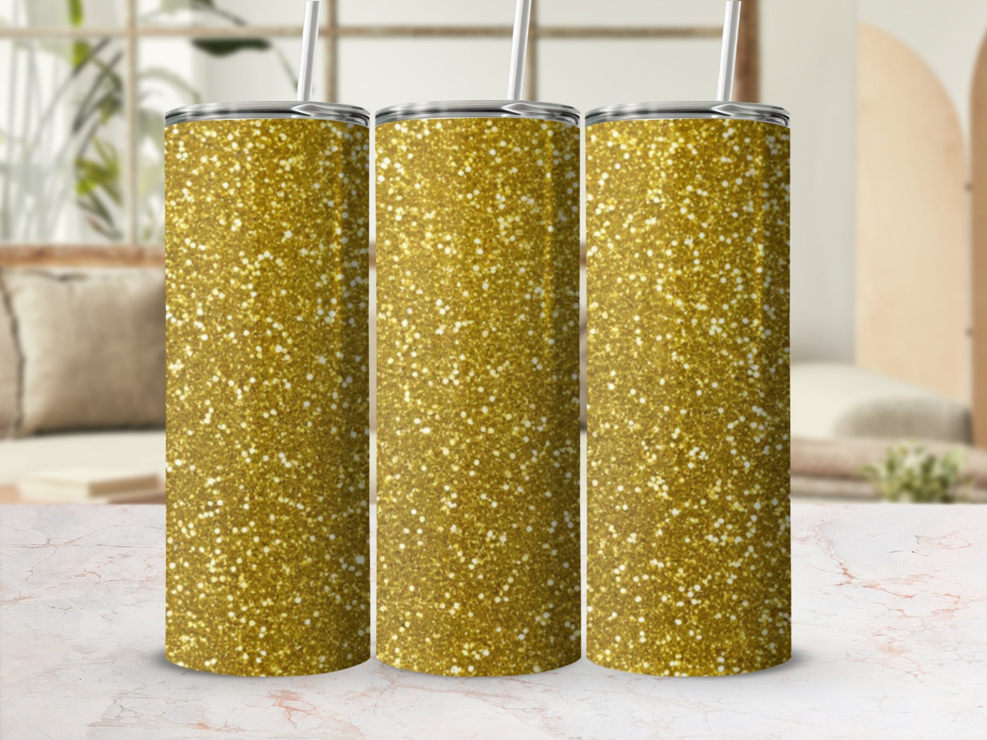 Three gold glitter tumblers with straws on a marbled surface.