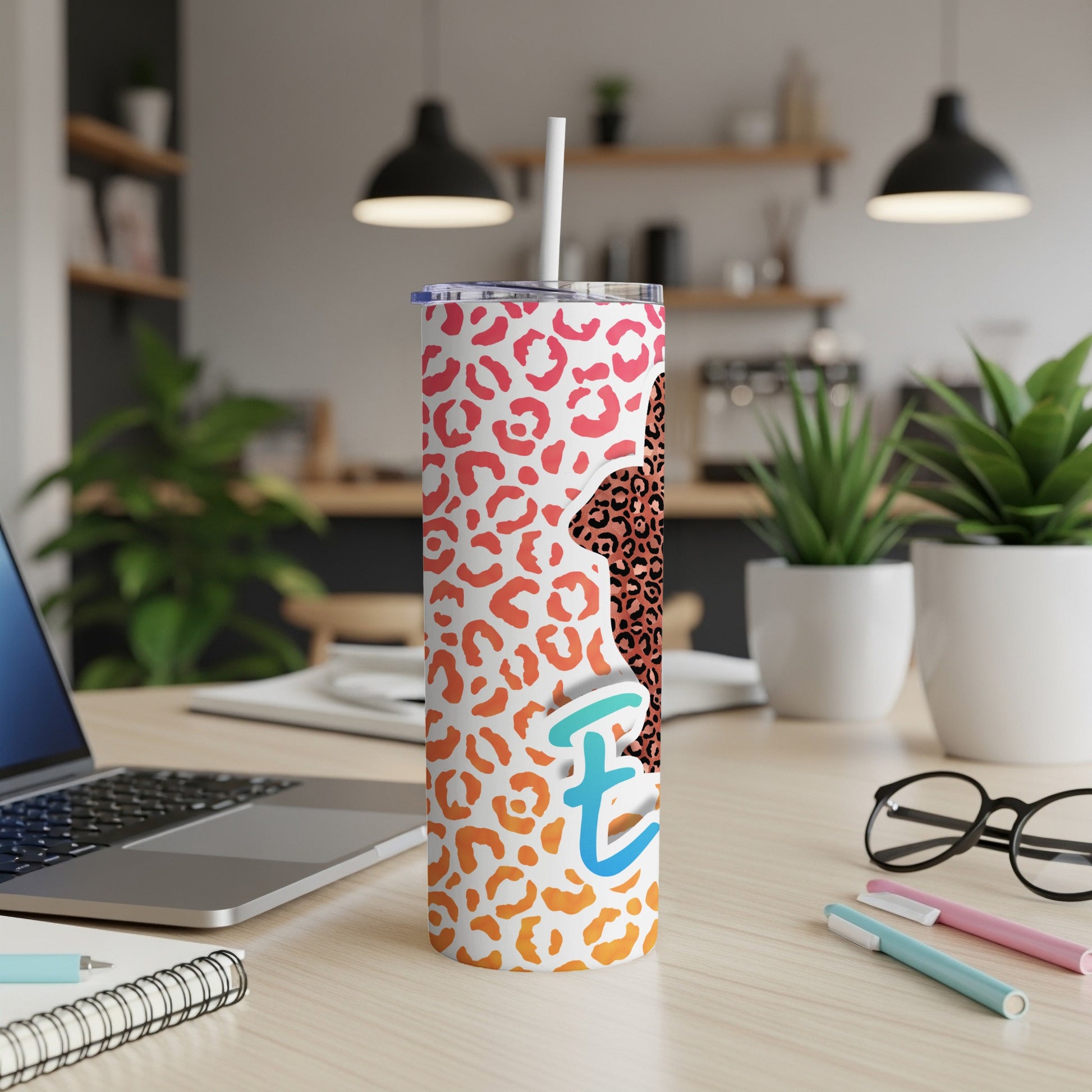 Leopard print tumbler with "Te" in blue and orange on a desk.